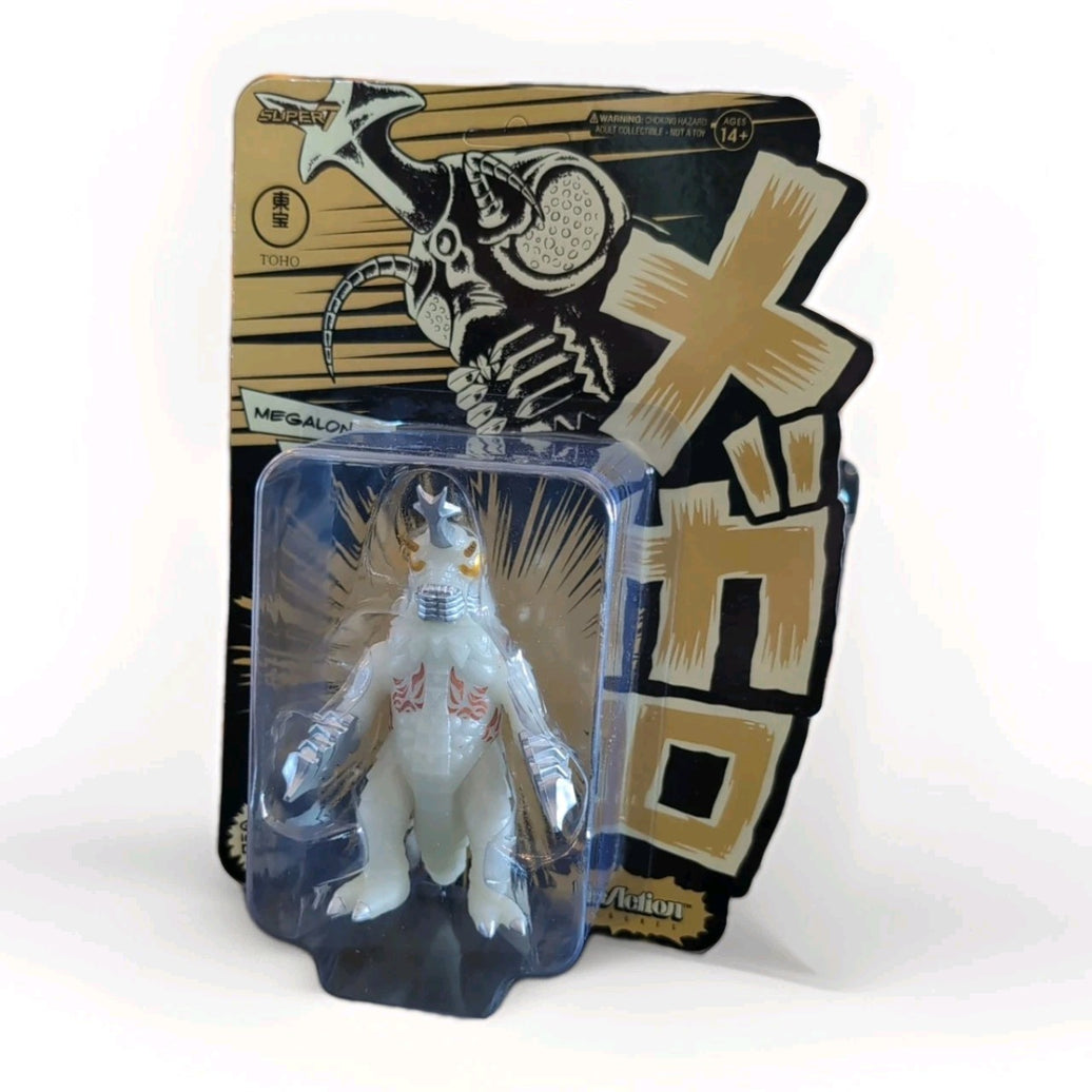 Super7 Megalon 1973 glow-in-the-dark Godzilla figure in original blister packaging with bold Japanese text background