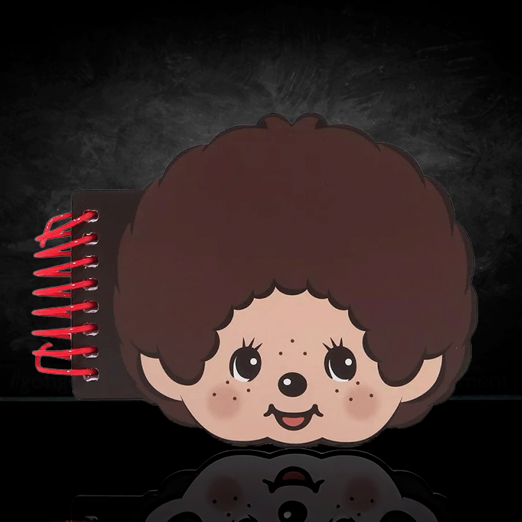 Go Figment Monchhichi die-cut spiral notebook shaped like smiling character face with curly hair on black background