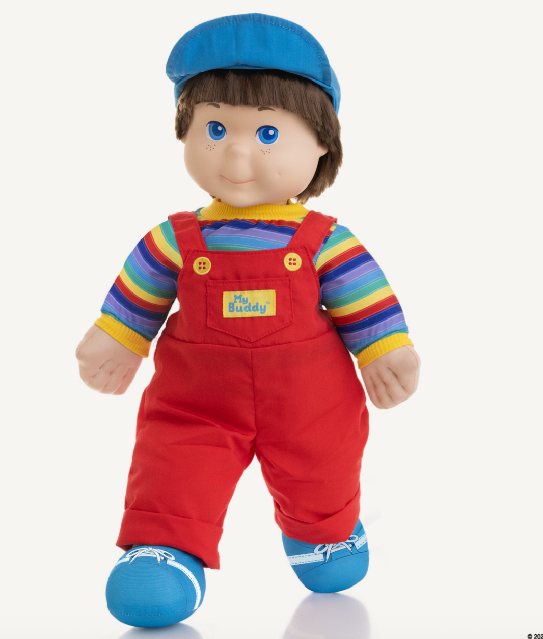 Playskool My Buddy doll wearing red overalls, rainbow shirt, blue hat and shoes, standing against white background.