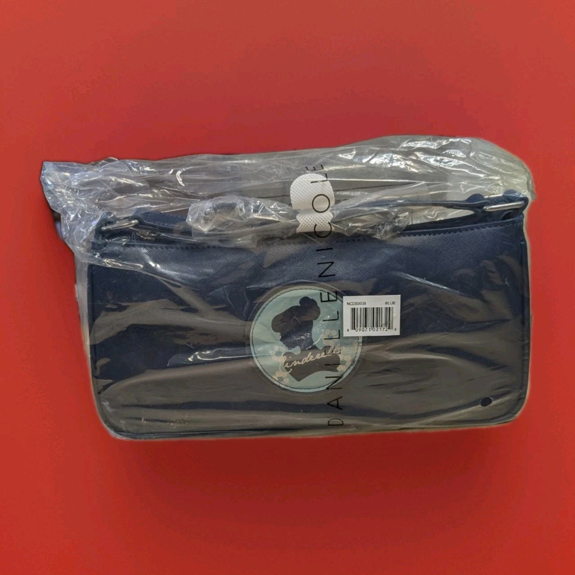Danielle navy blue baguette bag featuring Cinderella silhouette patch and barcode label in clear protective plastic wrap on red surface