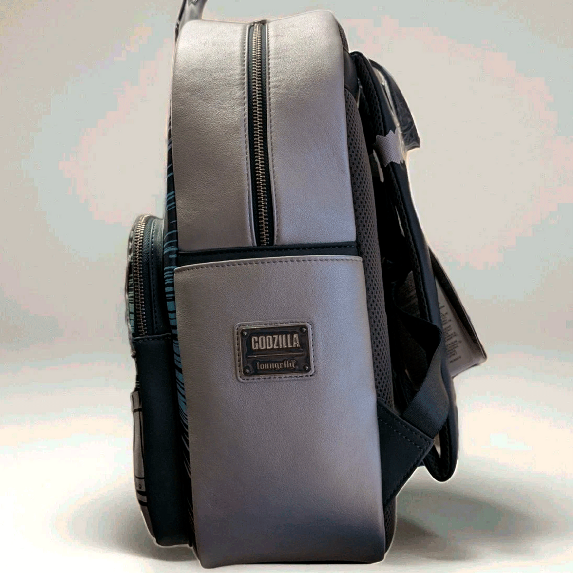 Side view of Loungefly full-size backpack in metallic finish with Godzilla logo patch and black straps visible