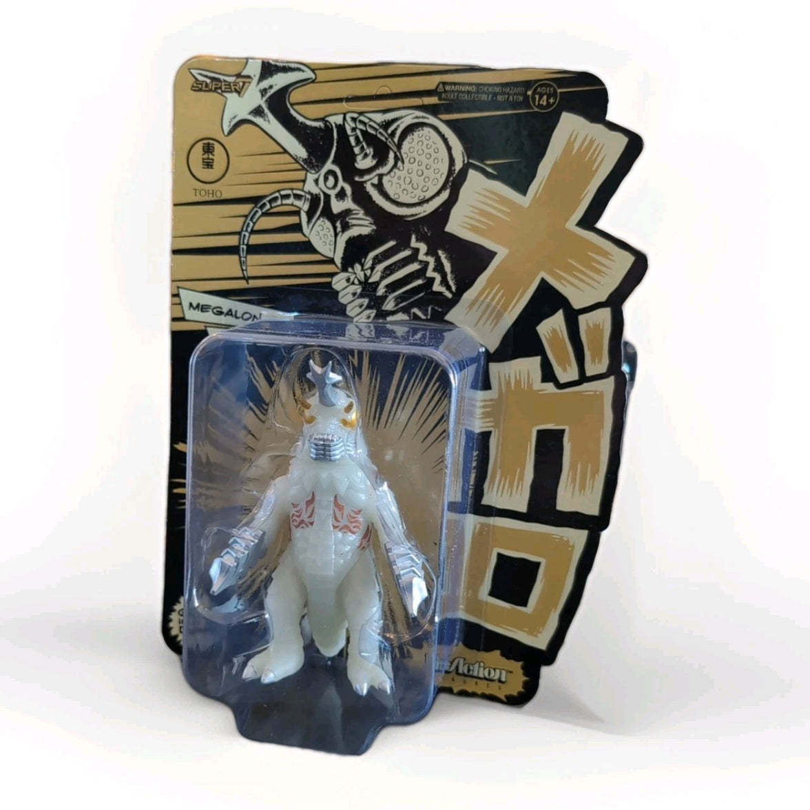 Super7 Megalon 1973 glow-in-the-dark Godzilla figure in original blister packaging with bold Japanese text background