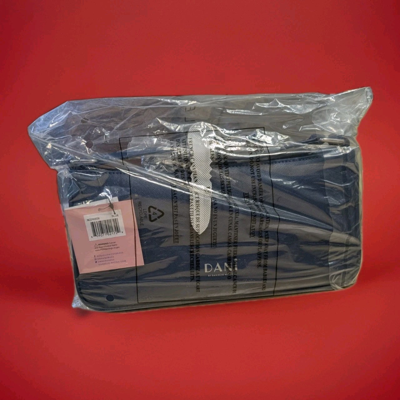 Danielle navy blue handbag in protective plastic with barcode and care label on red background