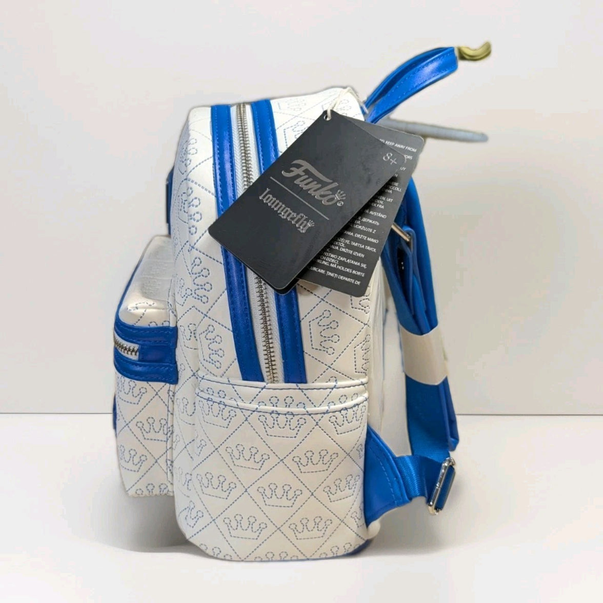 Loungefly mini backpack in white vegan leather with blue crown stitching and dual zipper side view showing tags and adjustable straps