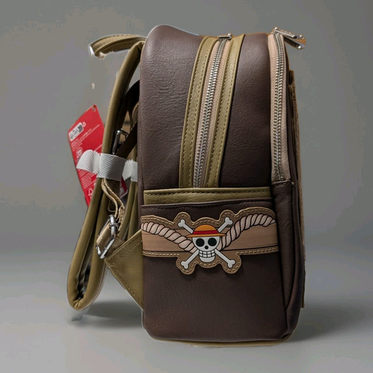 Side view of Loungefly mini backpack with Monkey D. Luffy pirate skull emblem on brown and tan faux leather