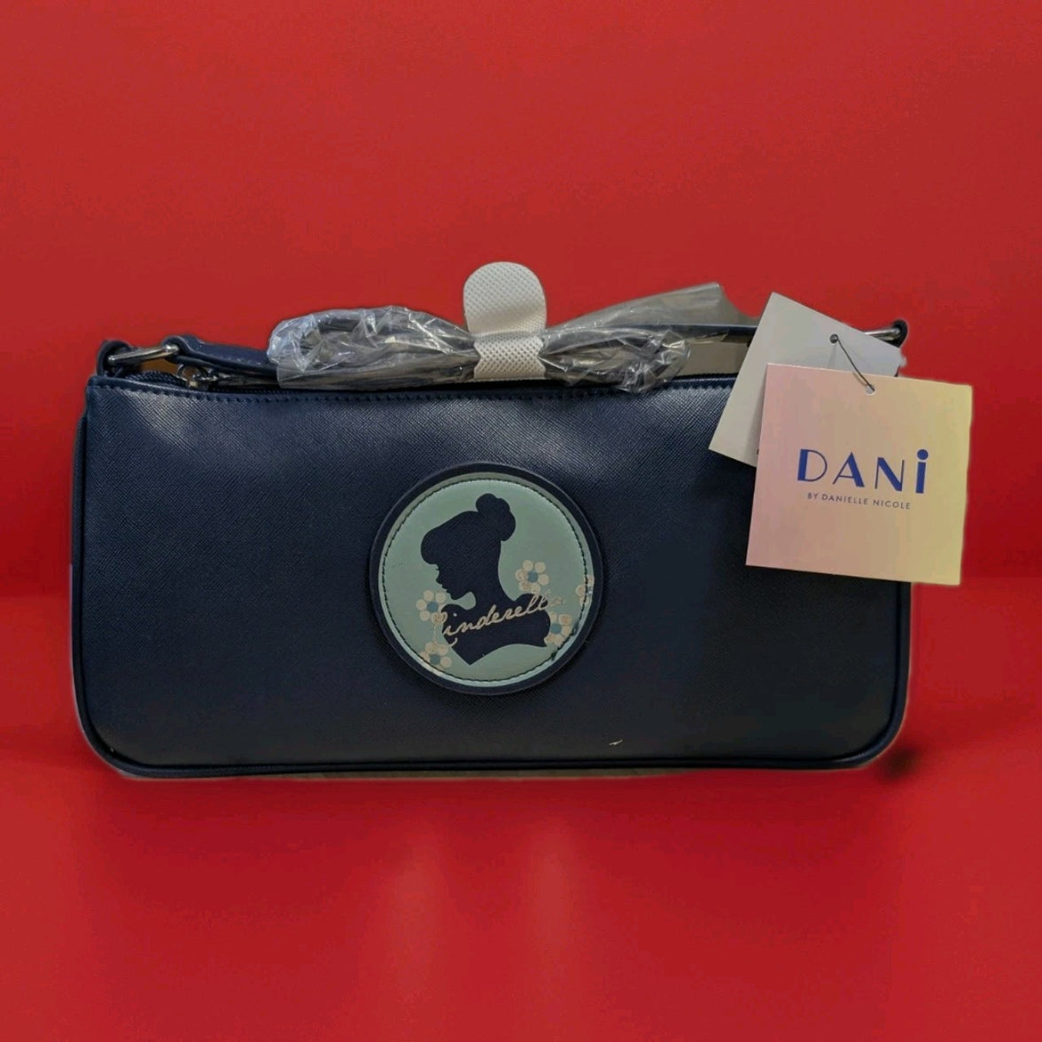 Danielle navy baguette bag with Cinderella silhouette patch and floral accents on front against red background