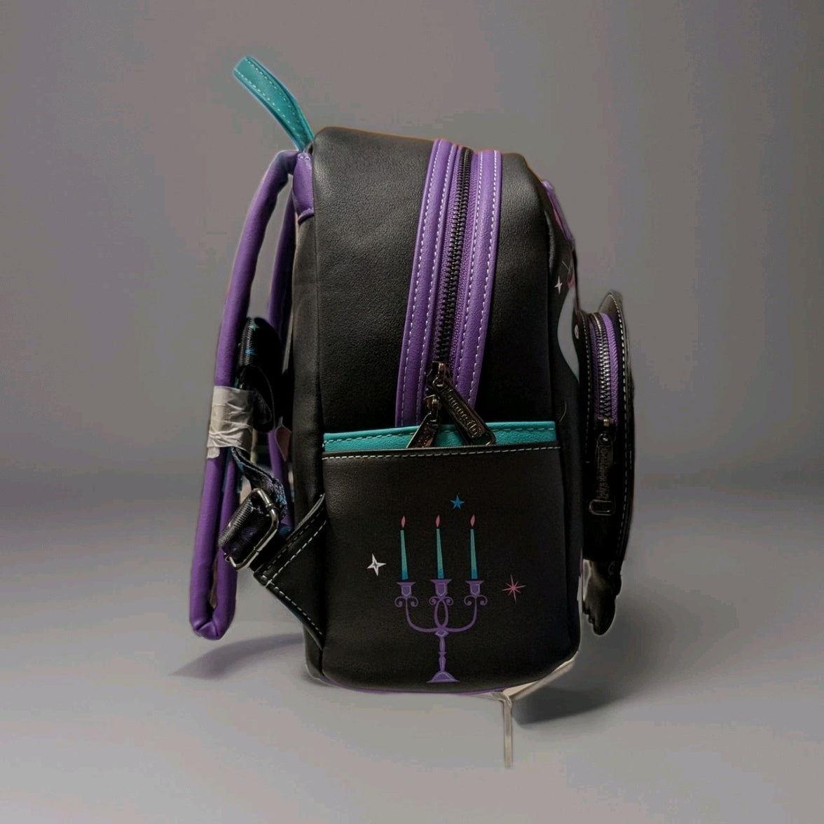 Side view of Loungefly mini backpack with purple zippers, teal accents, and Haunted Mansion candelabra design on black faux leather