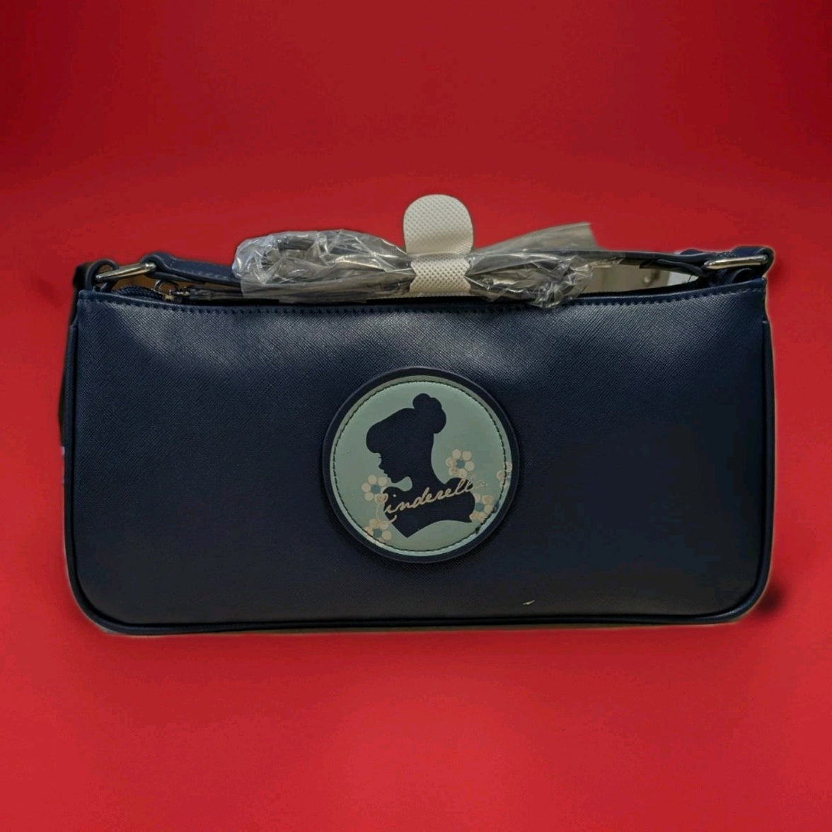 Danielle navy crossbody bag with Cinderella silhouette patch and floral details on front against red background