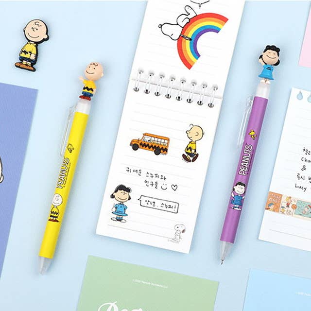 K-Wonderland Peanuts ballpoint pens in yellow and purple with Snoopy and Friends character toppers on pastel background