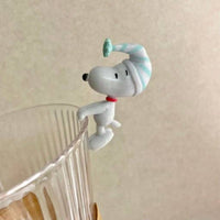 K-Wonderland Peanuts Snoopy blind box figure wearing striped nightcap perched on rim of clear textured glass