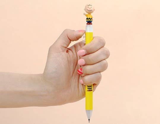 K-Wonderland Peanuts ballpoint pen in yellow with detailed Charlie Brown figure topper held in hand on plain background