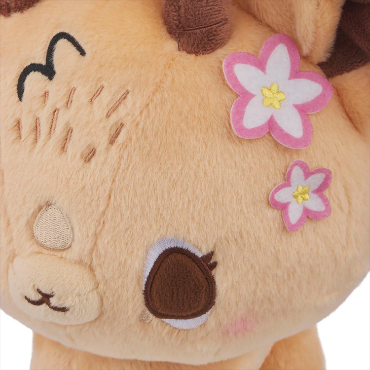 Close-up of a soft plush toy with embroidered eyes and pink and white felt flowers on its head.