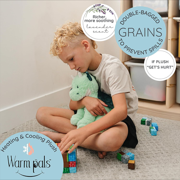 Child sitting on floor playing with blocks while holding a soft green microwavable lavender scented dragon plush toy