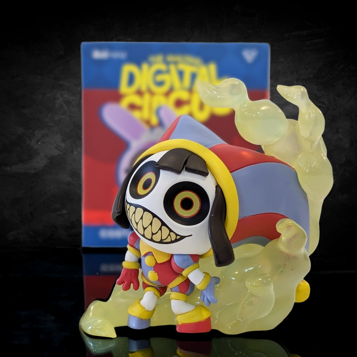 Glitch Animiniz figure from Digital Circus wearing a colorful jester hat with large eyes and sharp-toothed grin surrounded by yellow smoke