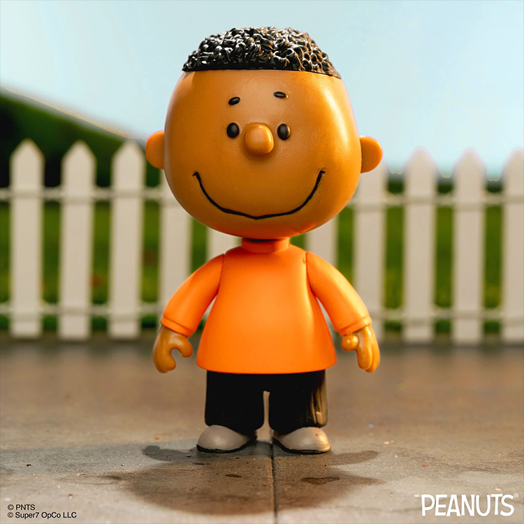 Franklin Peanuts action figure by Super7 in orange shirt, smiling, standing outdoors with white picket fence background.