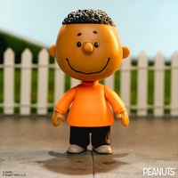 Franklin Peanuts action figure by Super7 in orange shirt, smiling, standing outdoors with white picket fence background.