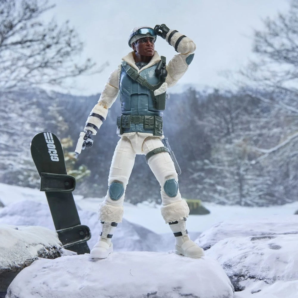 G I Joe action figure in arctic gear standing beside a snowboard in a snowy mountain landscape