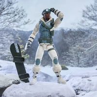 G I Joe action figure in arctic gear standing beside a snowboard in a snowy mountain landscape