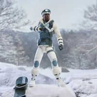 Action figure in white winter gear standing in a snowy landscape beside a snowboard