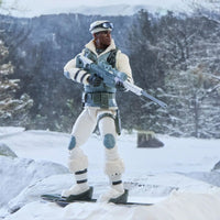 Action figure in white winter gear holding a rifle while standing on skis in a snowy mountain landscape