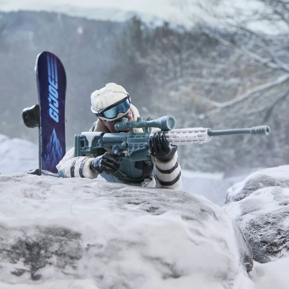 Toy soldier wearing winter gear and goggles, aiming a rifle from behind snow covered rocks with a ski nearby