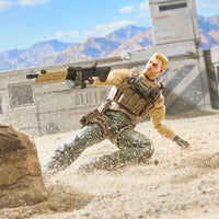 Action figure soldier sliding through sand with a rifle against a desert mountain backdrop