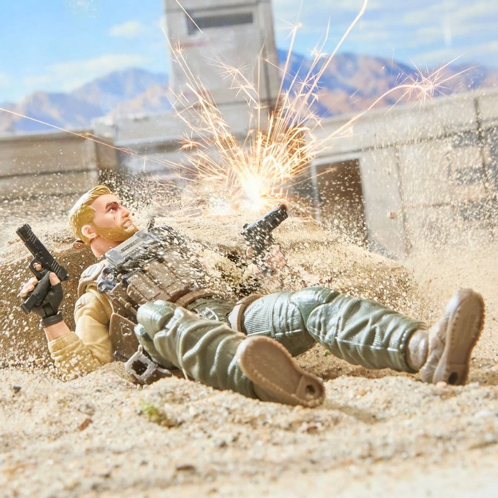 Two military action figures lie in sand as sparks burst behind them