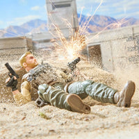 Two military action figures lie in sand as sparks burst behind them