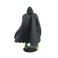 Back view of a small green-legged figure wearing a black hooded cloak on a display base