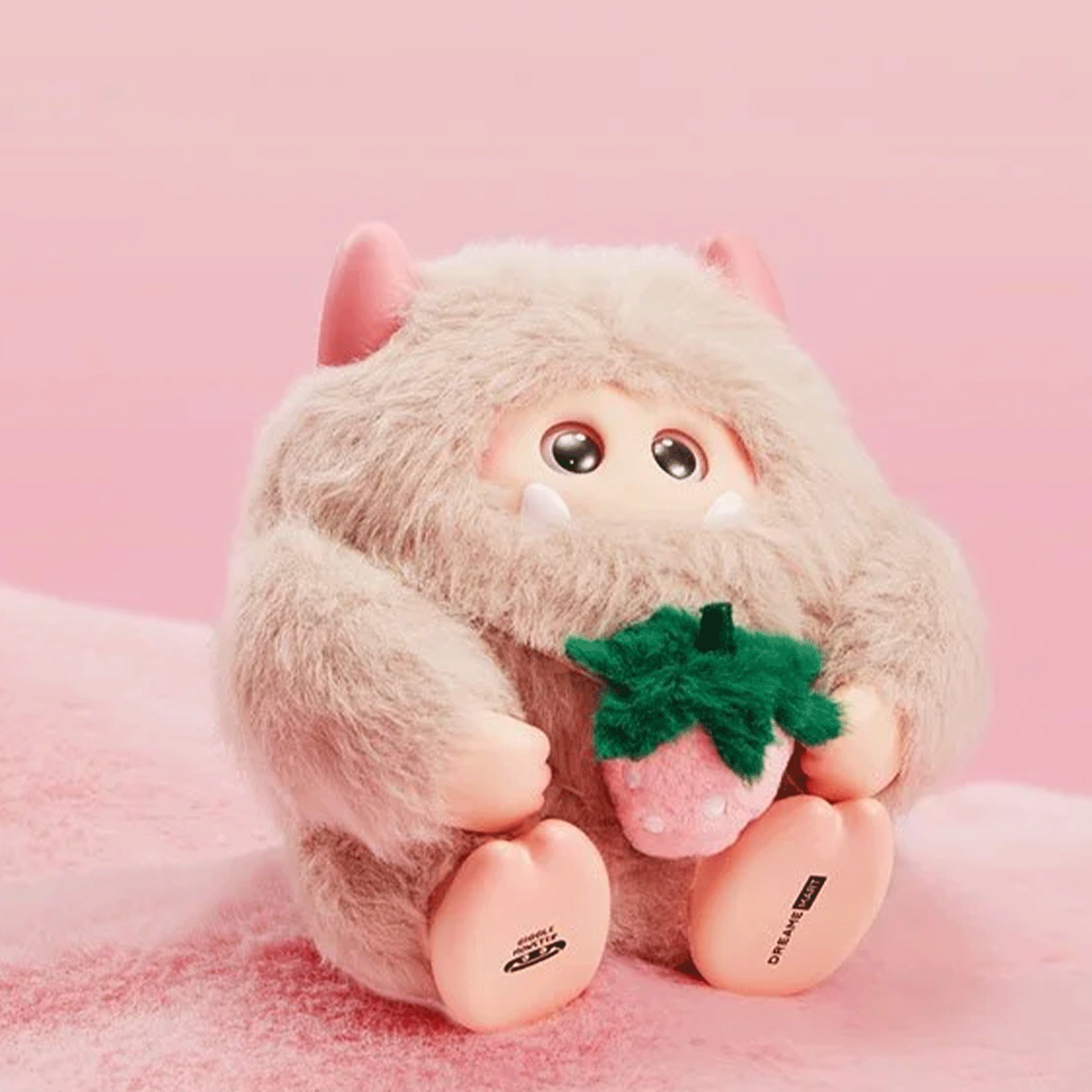 OHKU Giggle Monster Marshmallow Dreams plush with cream fur holding a green strawberry on soft pink surface