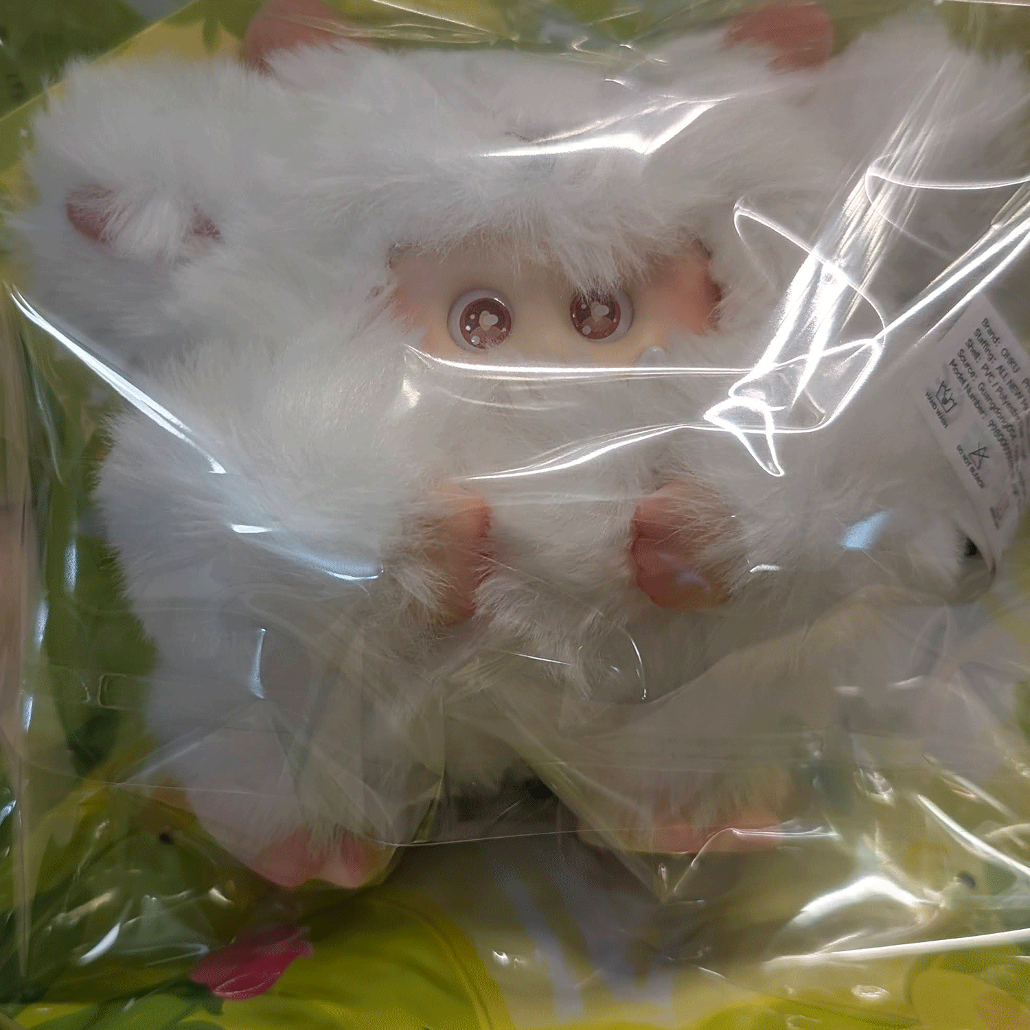 OHKU Giggle Monster vinyl plush with large eyes and fluffy white fur, inside clear plastic blind box packaging