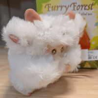 OHKU Giggle Monster plush in fluffy white woodland creature costume with round eyes and small horns on wooden surface