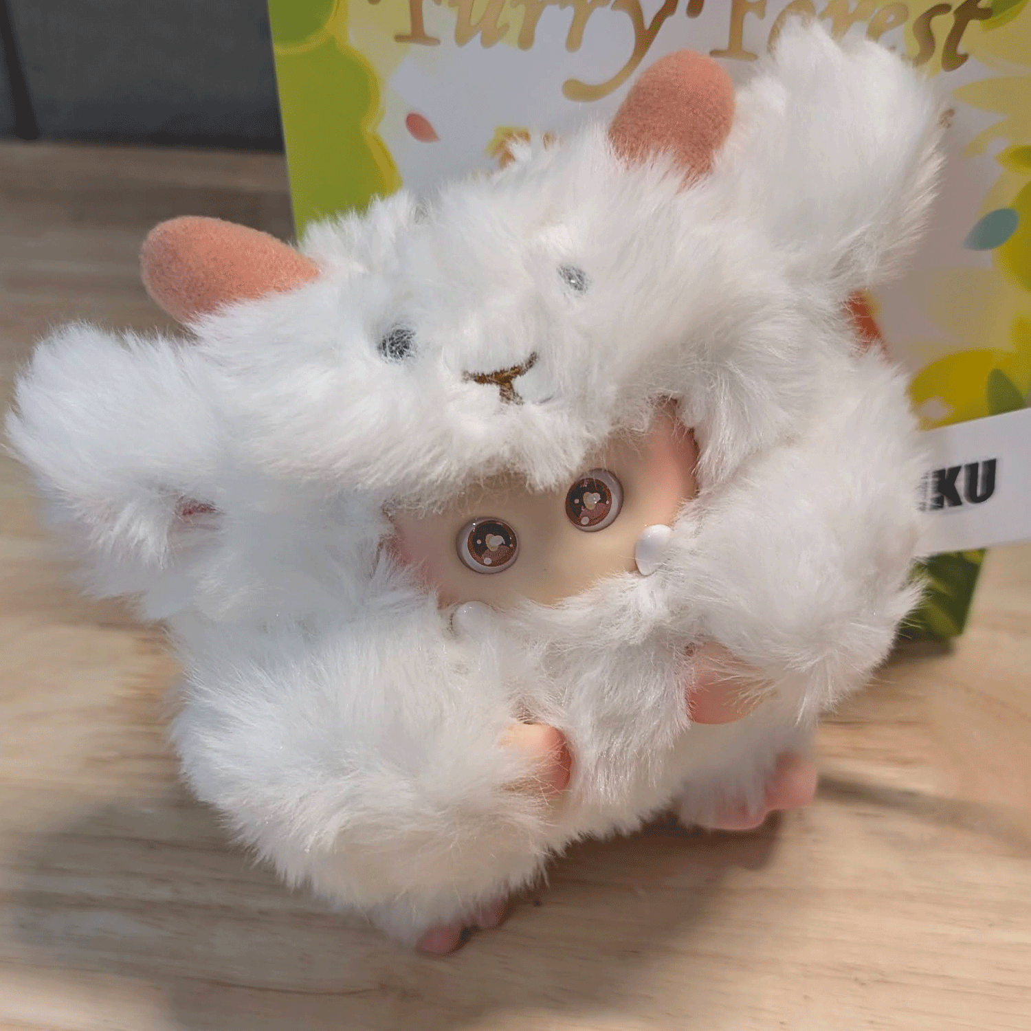 OHKU Giggle Monster vinyl plush in fluffy white creature costume with tiny fangs and sparkling eyes on wooden surface
