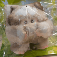 OHKU Giggle Monster plush in soft brown and cream furry creature suit with wide eyes inside clear packaging