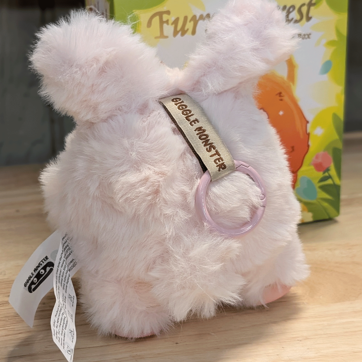 OHKU Giggle Monster Furry Forest plush figure in pale pink fluffy costume with keychain ring on wooden surface