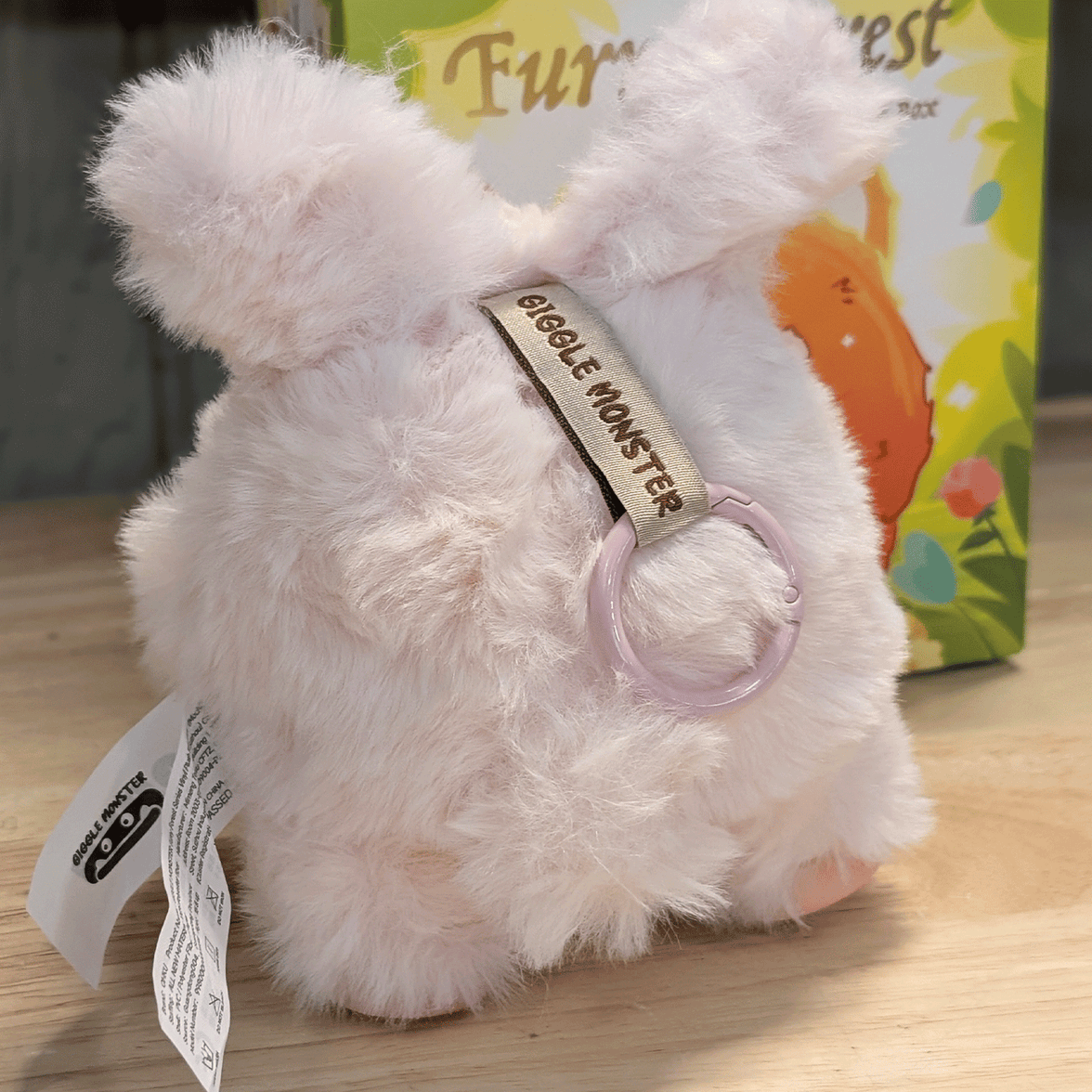 OHKU Giggle Monster Furry Forest plush figure in pale pink fluffy costume with keychain ring on wooden surface