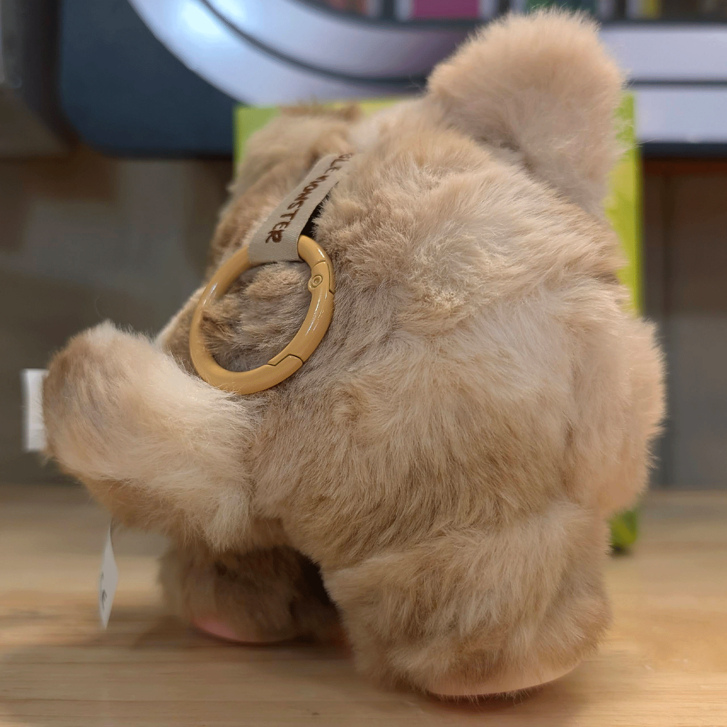 OHKU Giggle Monster plush in soft beige fuzzy creature suit with plastic loop keychain attached on wooden surface