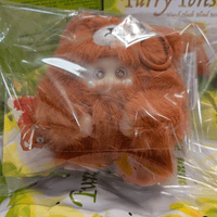 OHKU Giggle Monster plush figure in fuzzy rust-colored bear costume with shiny round eyes inside clear packaging