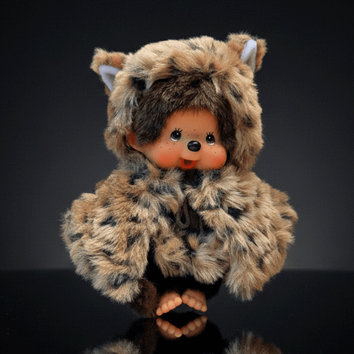 Sekiguchi 8-inch Monchhichi plush doll wearing leopard hood and cape with thumb in mouth on dark background