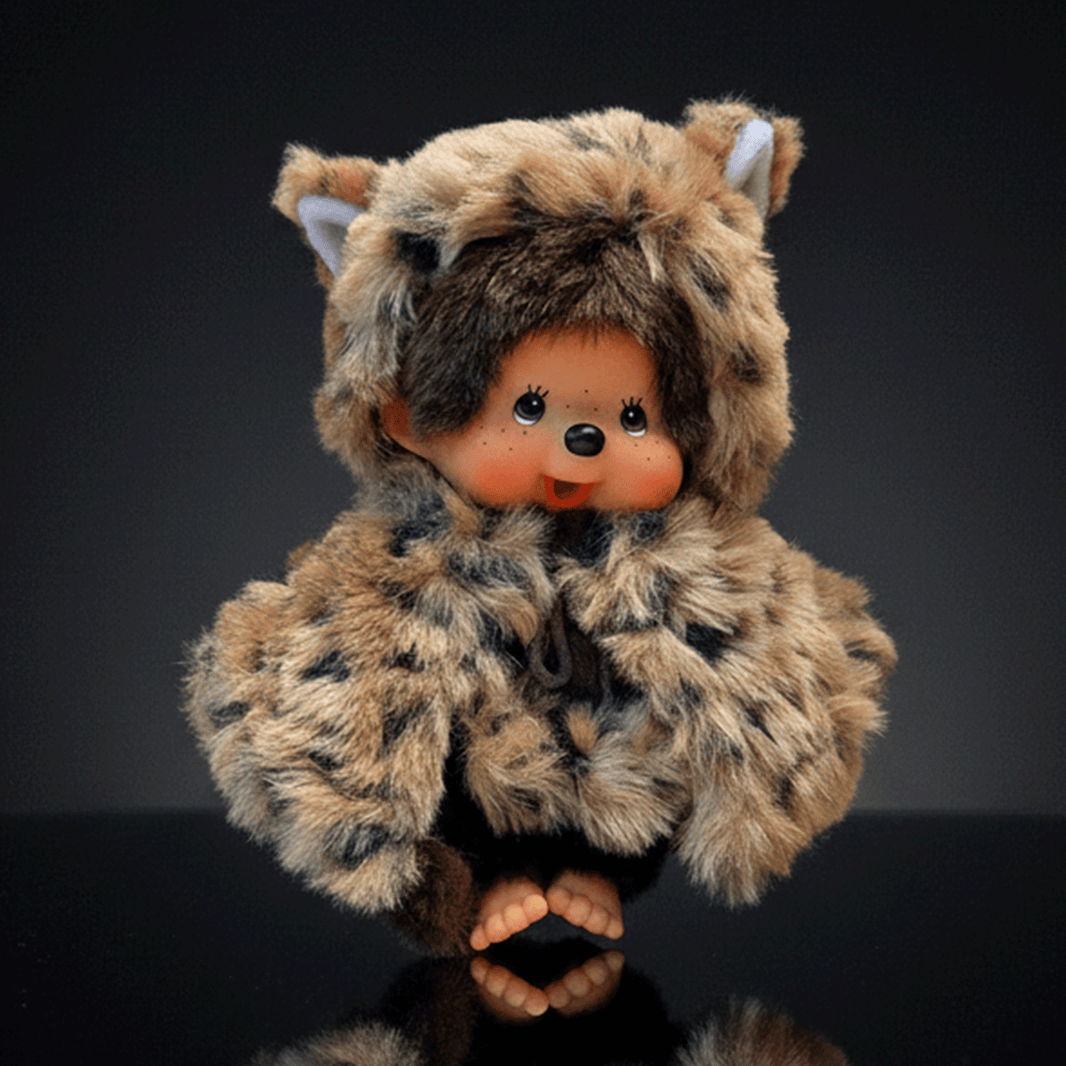 Sekiguchi 8-inch Monchhichi plush doll wearing leopard hood and cape with thumb in mouth on dark background