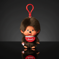 Monchhichi classic boy plush keychain with red bib and thumb in mouth hanging against dark background by Sekiguchi