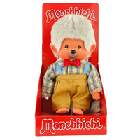 Monchhichi doll with white hair, red bow tie, plaid shirt, and yellow suspenders in red display box