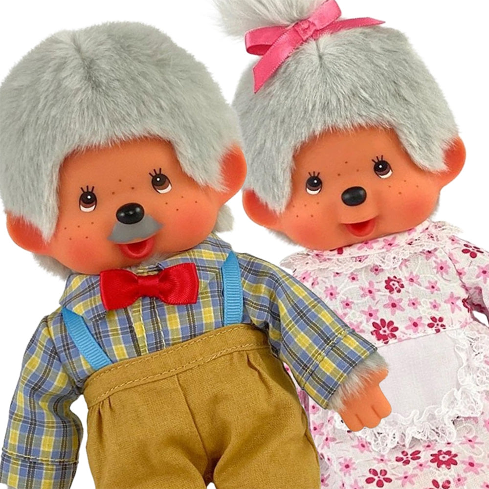 Two Monchhichi dolls with gray hair, one in plaid shirt and suspenders, the other in pink floral dress with a bow.