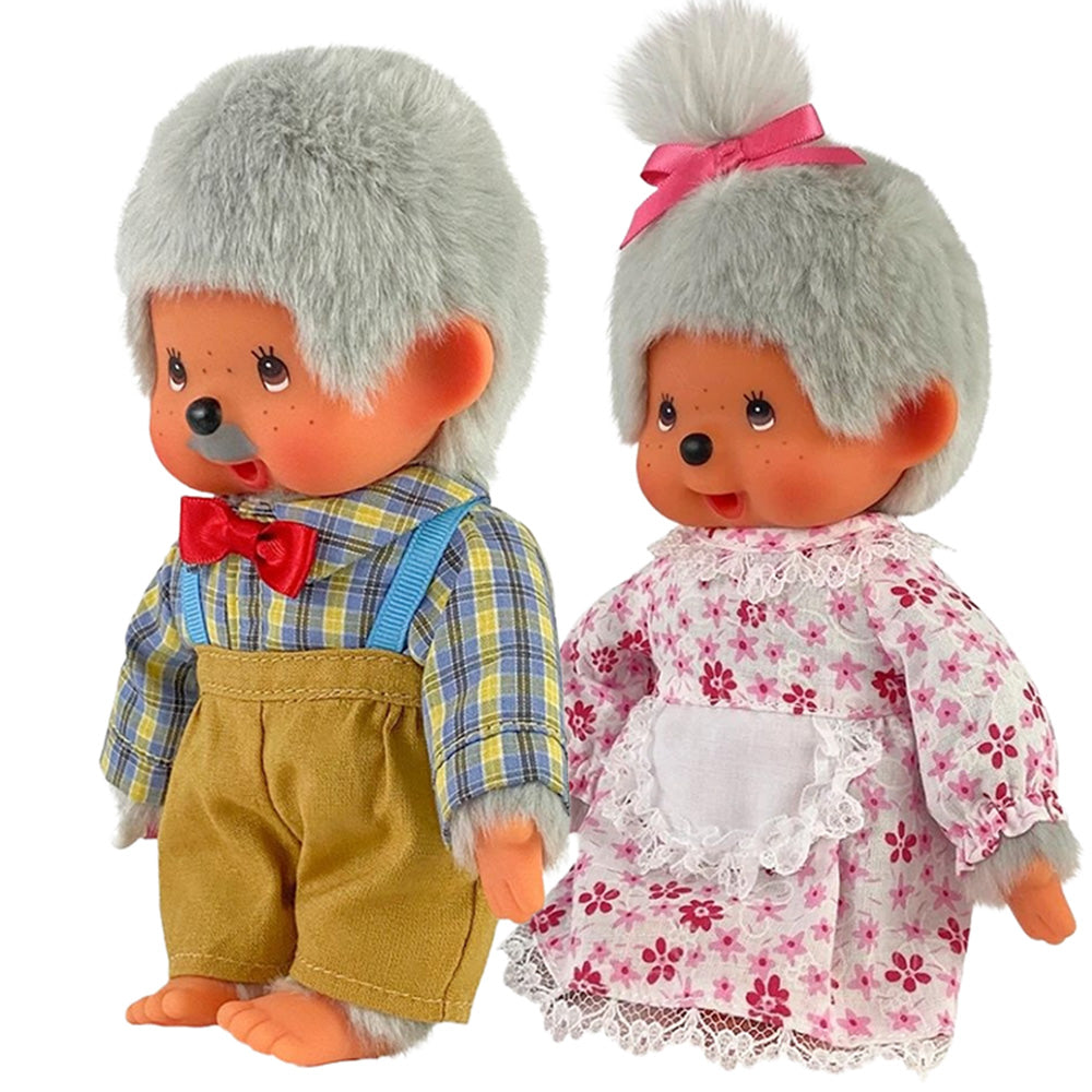 Two Monchhichi dolls, one in yellow overalls with red bow tie, the other in floral dress with pink ribbon and white apron.