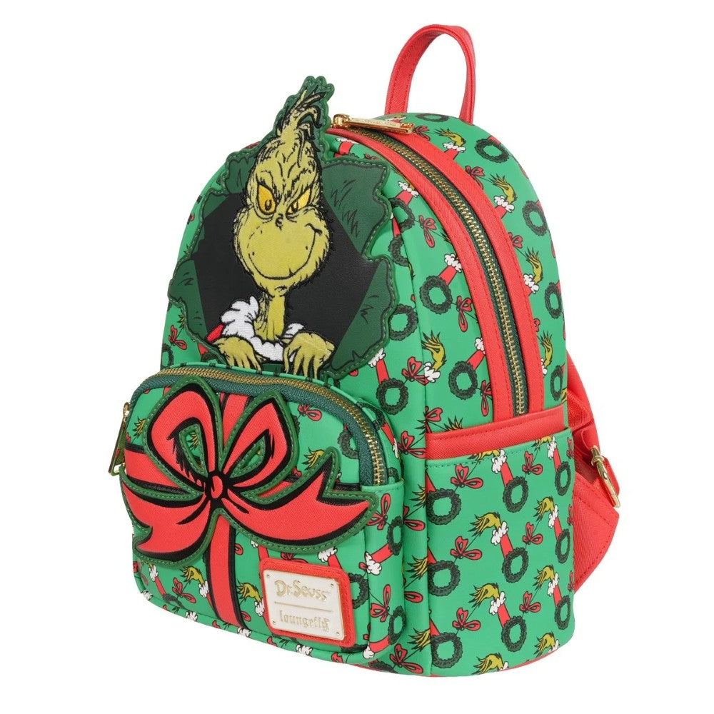Loungefly mini-backpack featuring Grinch peeking through wreath with red bow and festive green holiday pattern