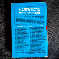 Vintage Hardy Boys mystery book back cover by Grosset & Dunlap featuring a blue bar and series titles list