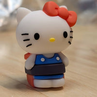 Go Figment Hello Kitty figure wearing blue outfit with red bow standing on wooden surface in soft focus background
