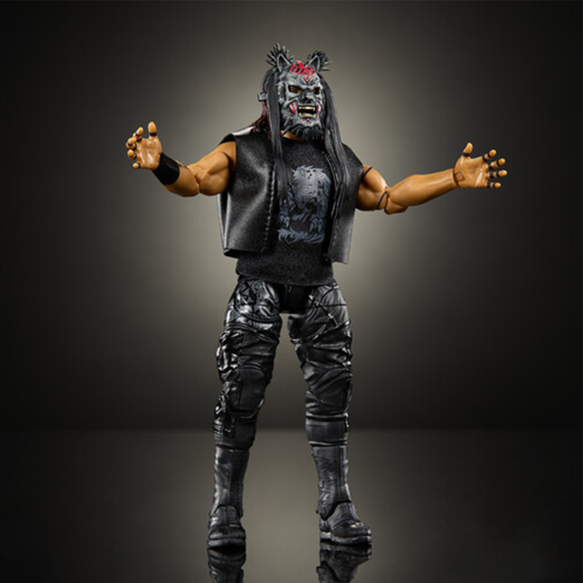 Black-clad action figure with a monster mask, long hair, armored pants, and outstretched arms against a dark background
