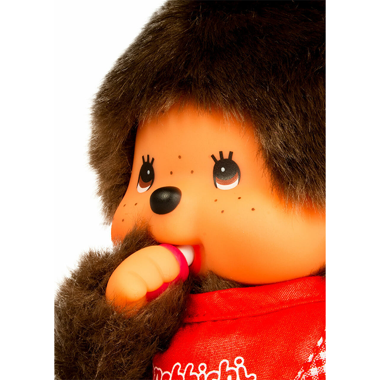 Close-up of Sekiguchi Monchhichi plush toy with red bib sucking thumb, showcasing soft fur and detailed face features.