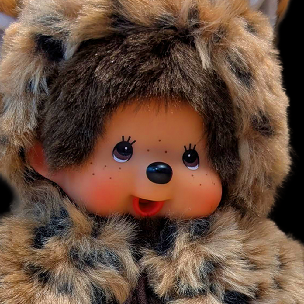 Sekiguchi Monchhichi plush wearing leopard print hood and cape with rosy cheeks and thumb in mouth close-up view